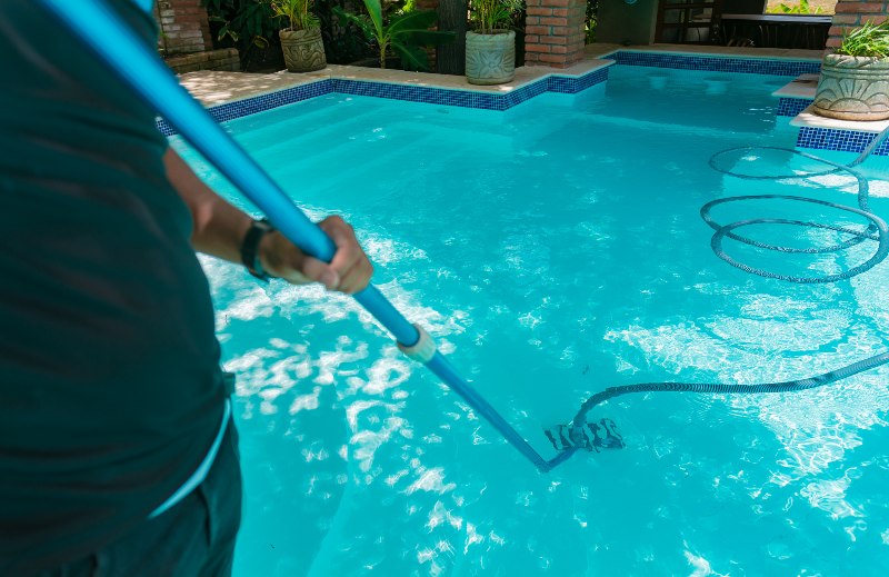 Man cleaning swimming pool with suction hose in VA & MD